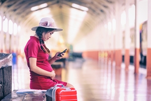 Pregnant person at a railway station with luggage.